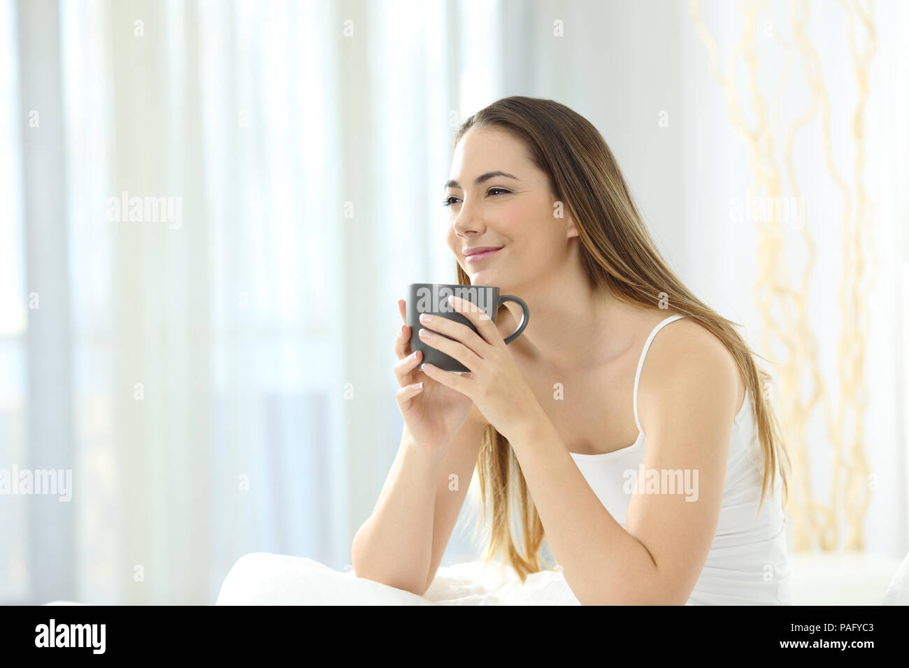 Ragazza rilassante svegliarsi avente la prima colazione al mattino cercando di distanza sul letto Foto Stock