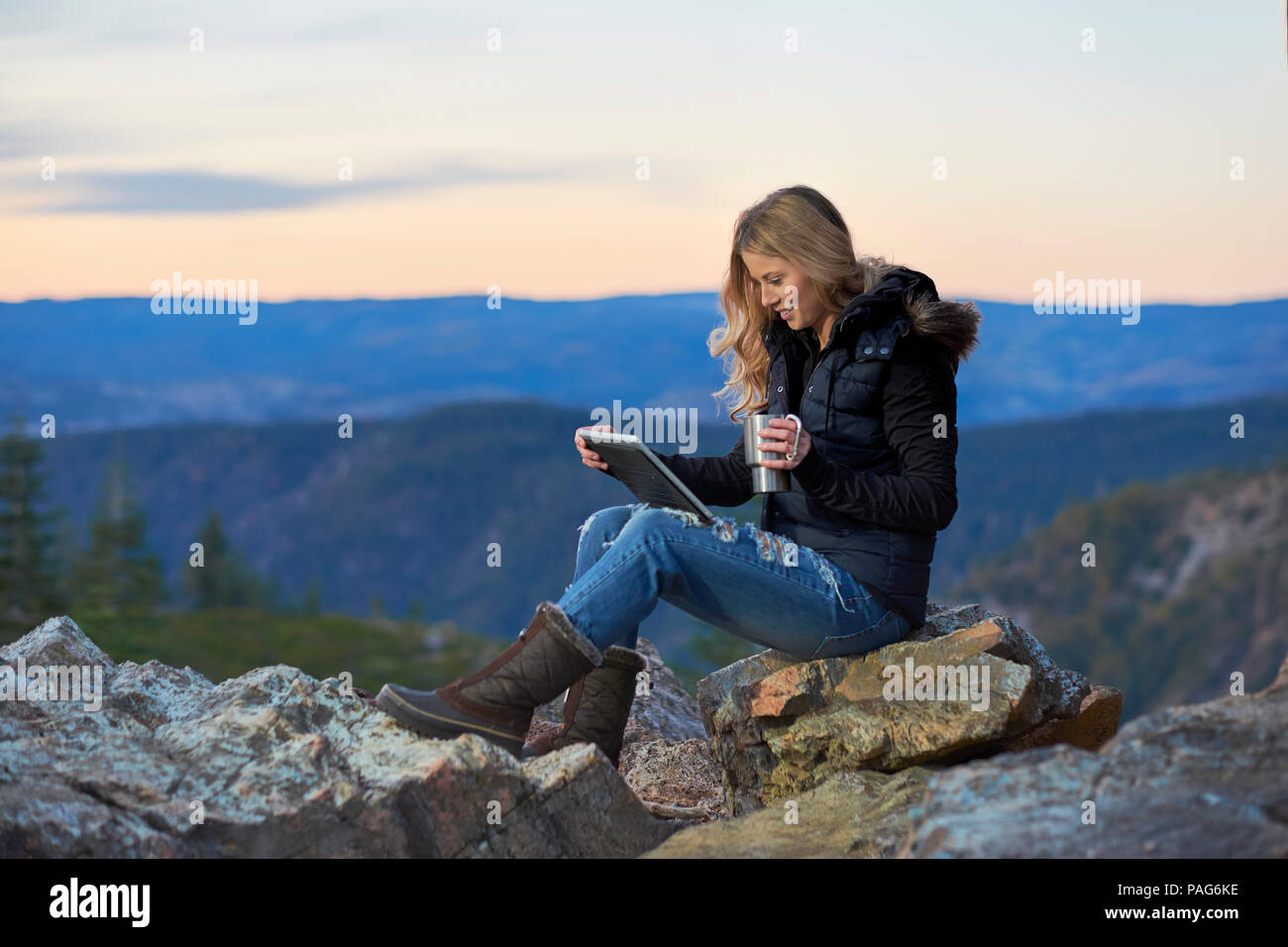 Un attraente donna millenario godendo la tecnologia mobile esterno durante il riposo dopo una escursione su di un crinale nelle montagne della Sierra Nevada. Foto Stock