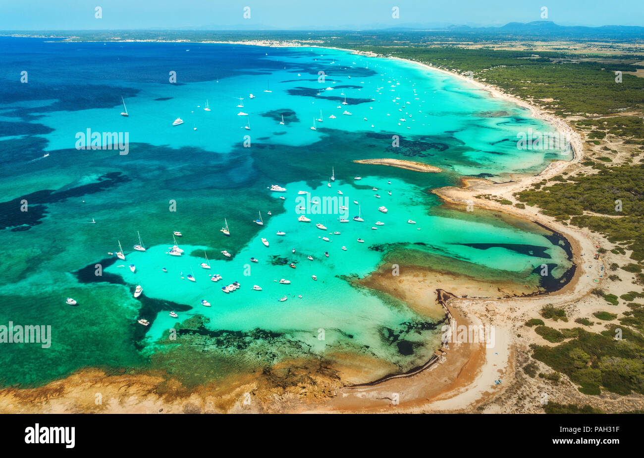 Vista aerea del mare trasparente con acqua blu, spiaggia sabbiosa, rocce, alberi verdi, yacht e barche nella mattina di sole in estate. Viaggiare a Maiorca, Bale Foto Stock