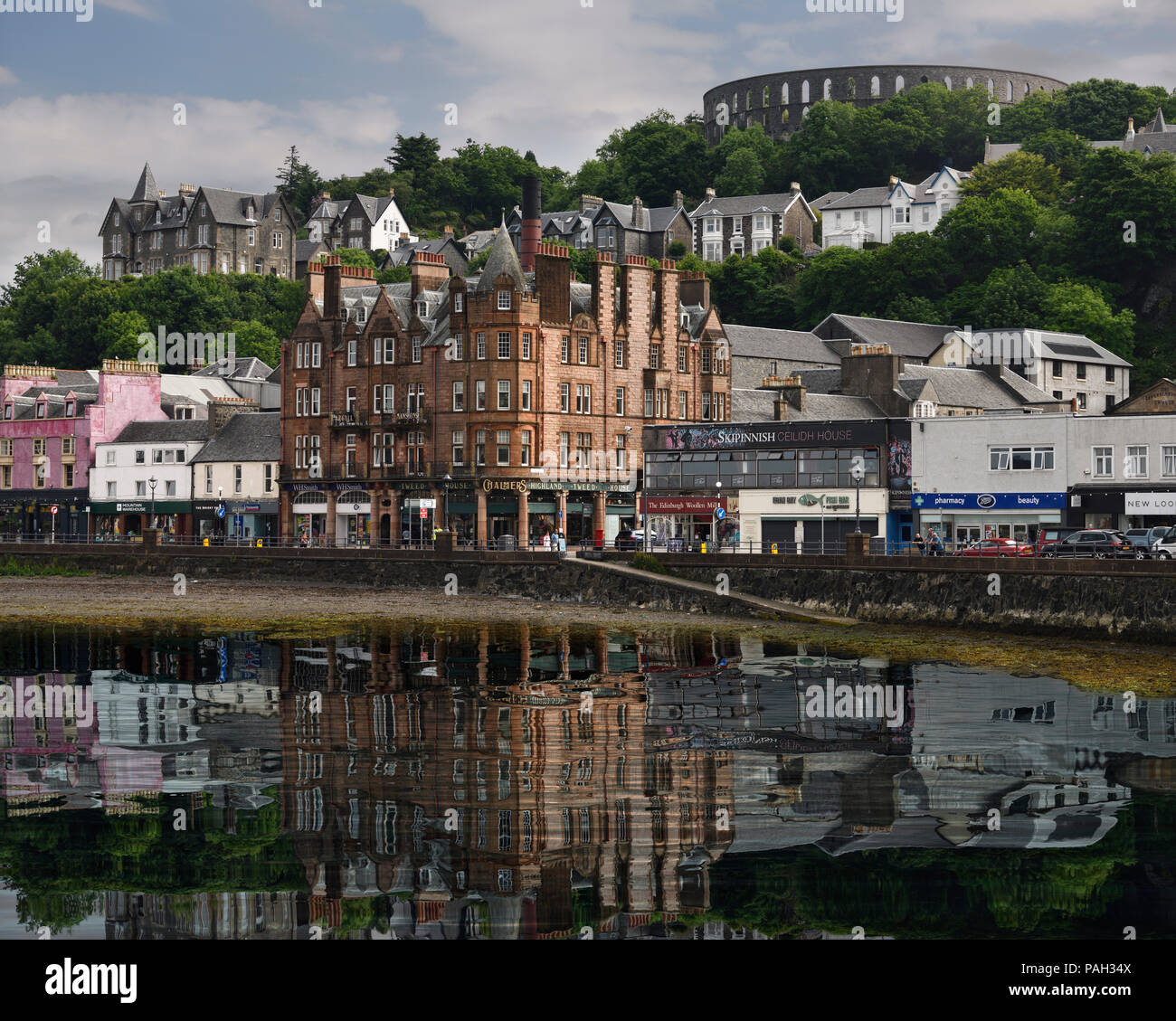 Edifici storici e McCaig's Tower Batteria sulla collina che si affaccia sul porto di Oban con acqua riflessioni in Oban Bay Scozia UK Foto Stock