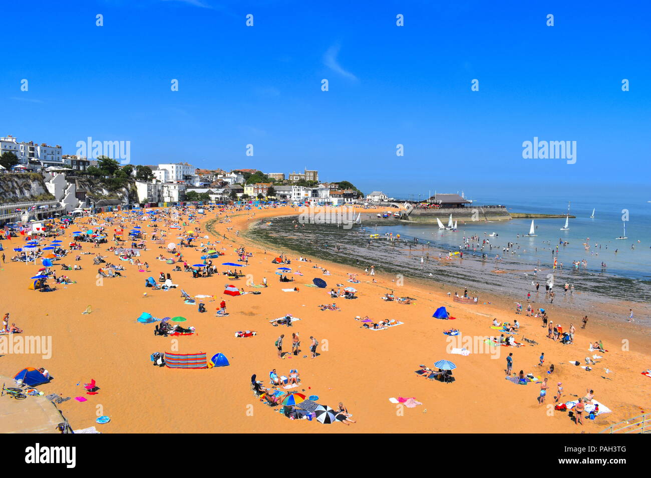 Inghilterra, Broadstairs. Pranzo Spiaggia con sun bagnanti durante la canicola estiva. Porto in background. Broadstairs, Kent, Regno Unito, Luglio 2018 Foto Stock