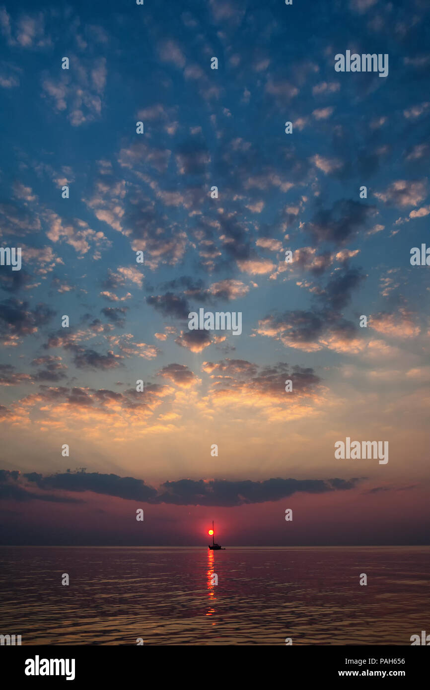 Il sole scende tra le onde del mare contro lo sfondo di yacht e nuvole all'orizzonte Foto Stock