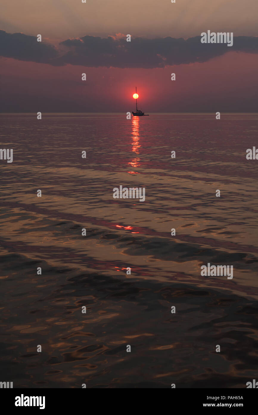 Il sole scende tra le onde del mare contro lo sfondo di yacht e nuvole all'orizzonte Foto Stock