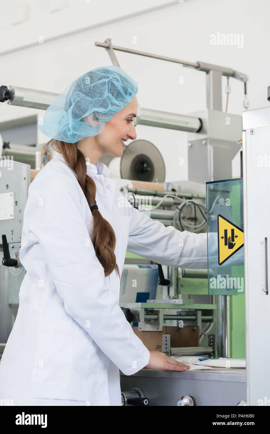 Donna ingegnere di produzione regolare le impostazioni di una macchina industriale Foto Stock