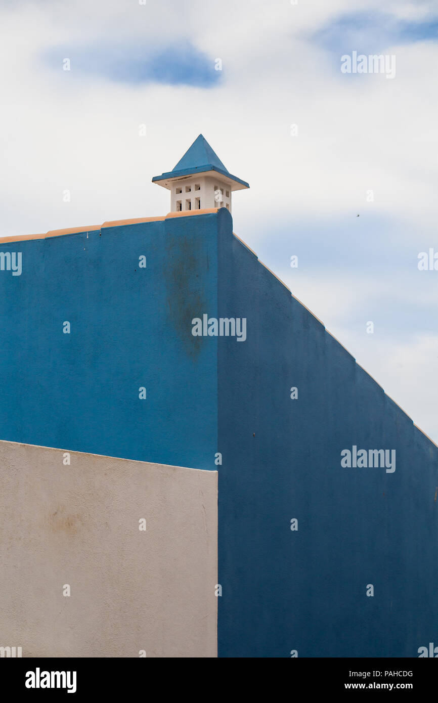 La parete laterale di una casa dipinta di bianco e due toni di blu. Tradizionale camino portoghese. Cielo nuvoloso abbinamento con la facciata. Lagos, Algarve, PORTOGALLO Foto Stock