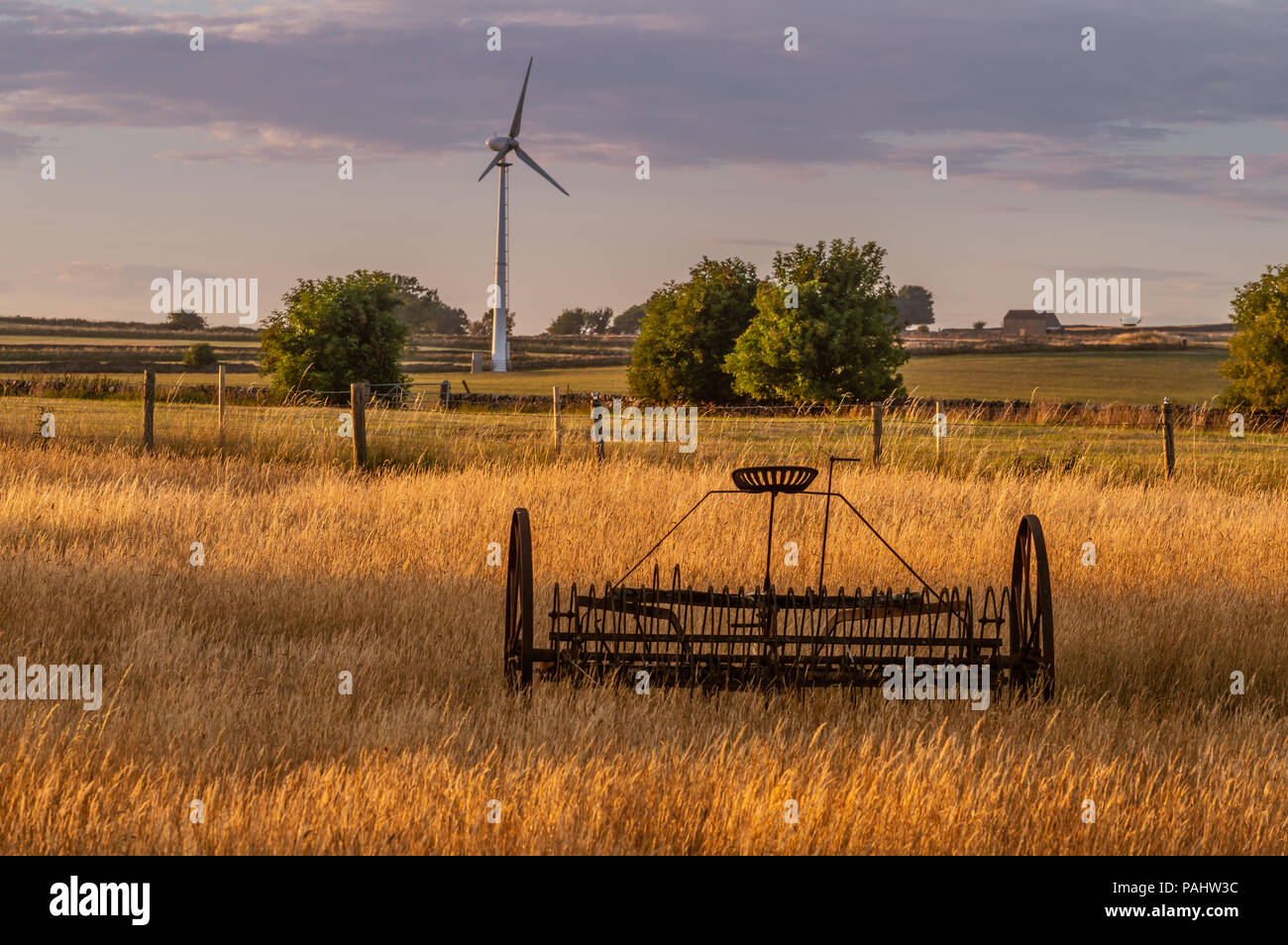 La vecchia e la nuova tecnologia. Il fieno rastrello e la turbina eolica in Staffordshire campo gli agricoltori al tramonto. Foto Stock