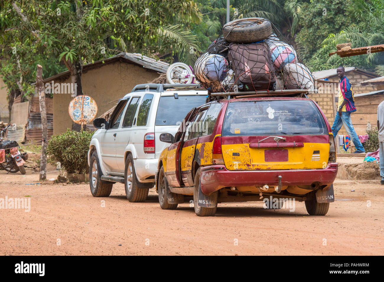 Due veicoli parcheggiare lungo la strada sterrata con bagagli e altri articoli per la casa impaccati saldamente sul tetto della vettura usurate, Repubblica di Guinea Foto Stock