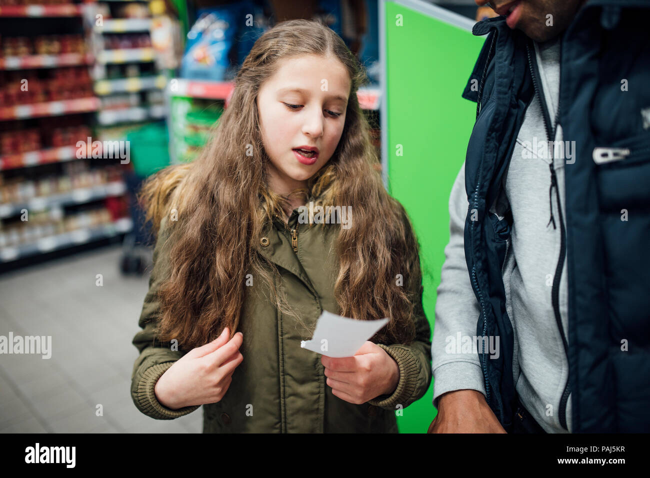 Bambina sta leggendo le cose da un elenco di acquisti a suo padre in un supermercato. Foto Stock