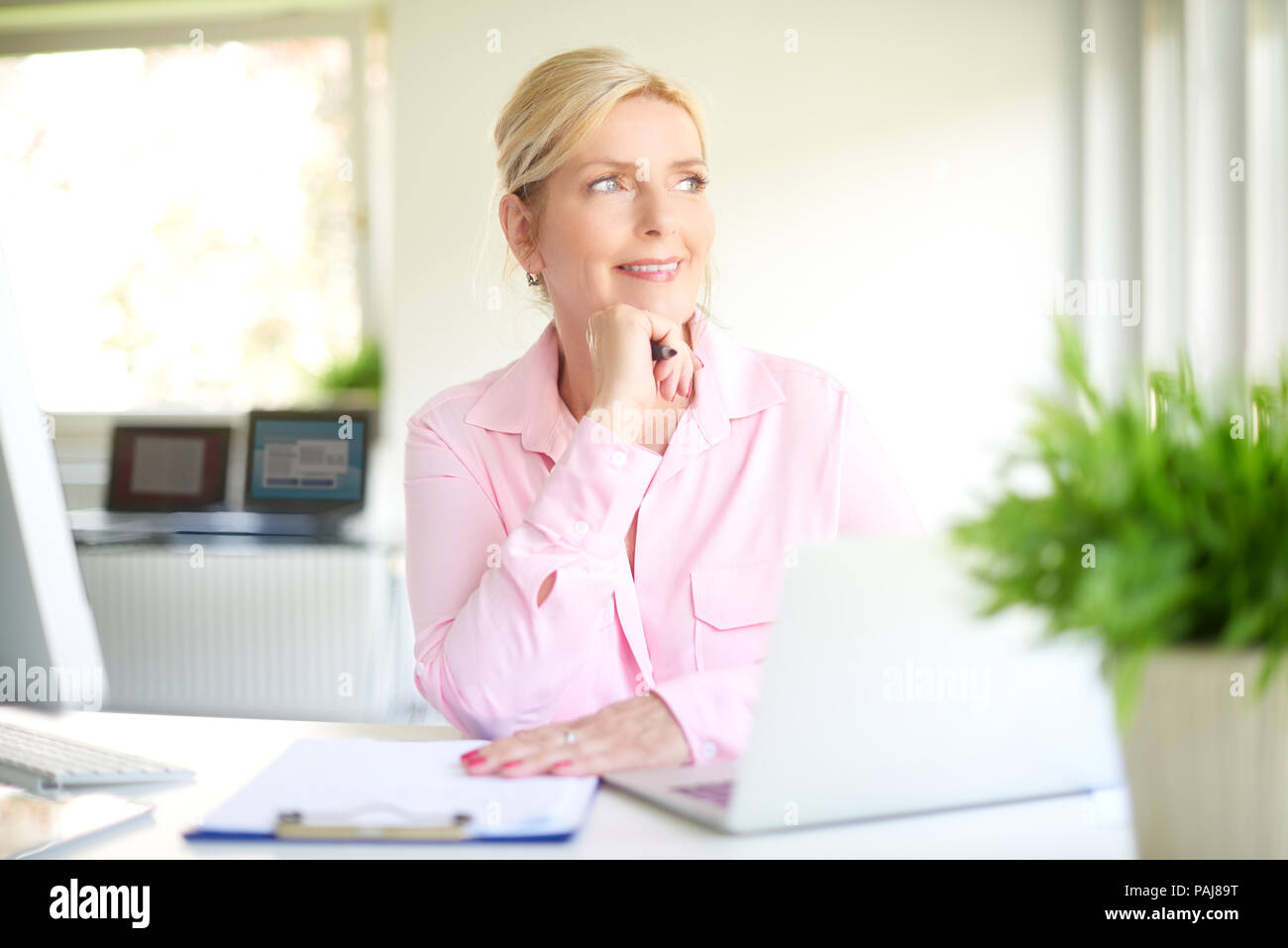 Pensando senior imprenditrice seduto alla scrivania in ufficio e guardando attraverso la finestra. Foto Stock