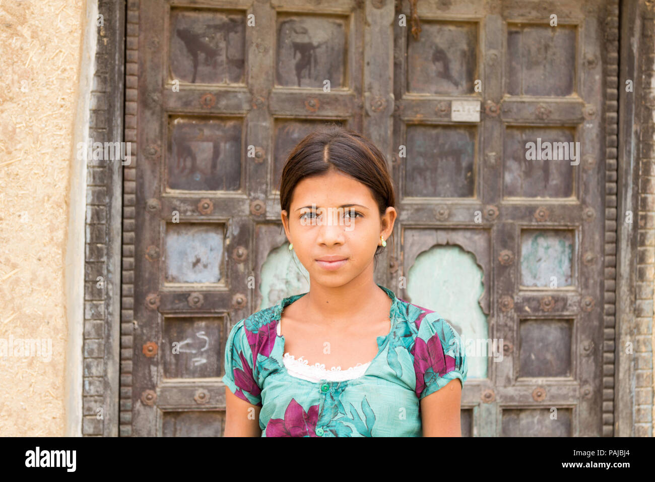 Giovane ragazza indiana in piedi al di fuori di una vecchia porta di legno in Shapura Bagh, Rajasthan. Foto Stock