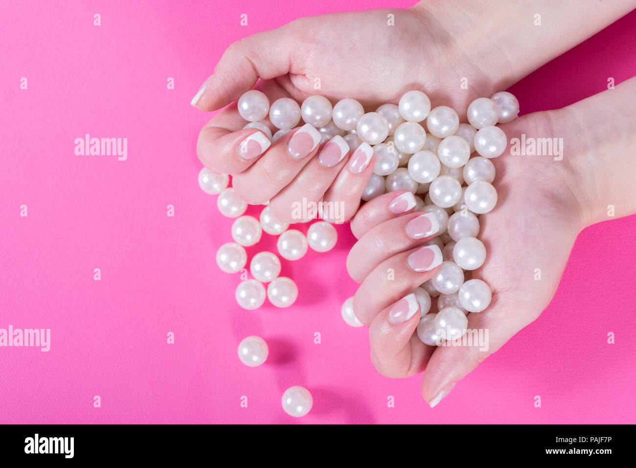 Giovani femmine tenendo molte perle in mano con Unghie french polish isolato su sfondo rosa. Manicure e femminilità concept Foto Stock