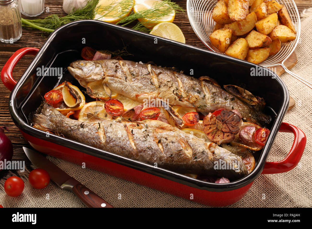 Pesce al forno con verdure e patate nella teglia su sfondo di legno Foto Stock