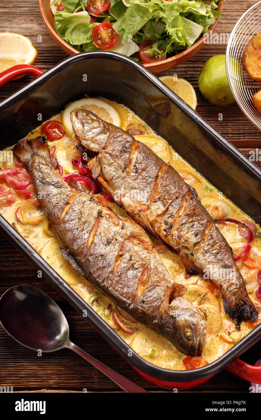 Pesce al forno con salsa di limone e le verdure in una padella Foto Stock