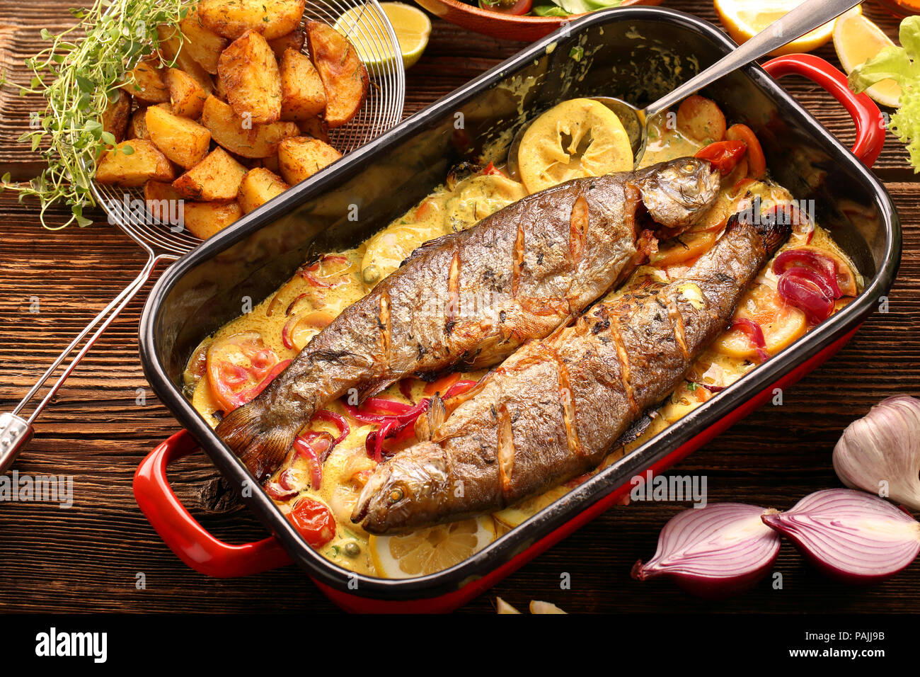 Pesce al forno con salsa di limone e le verdure in una padella Foto Stock