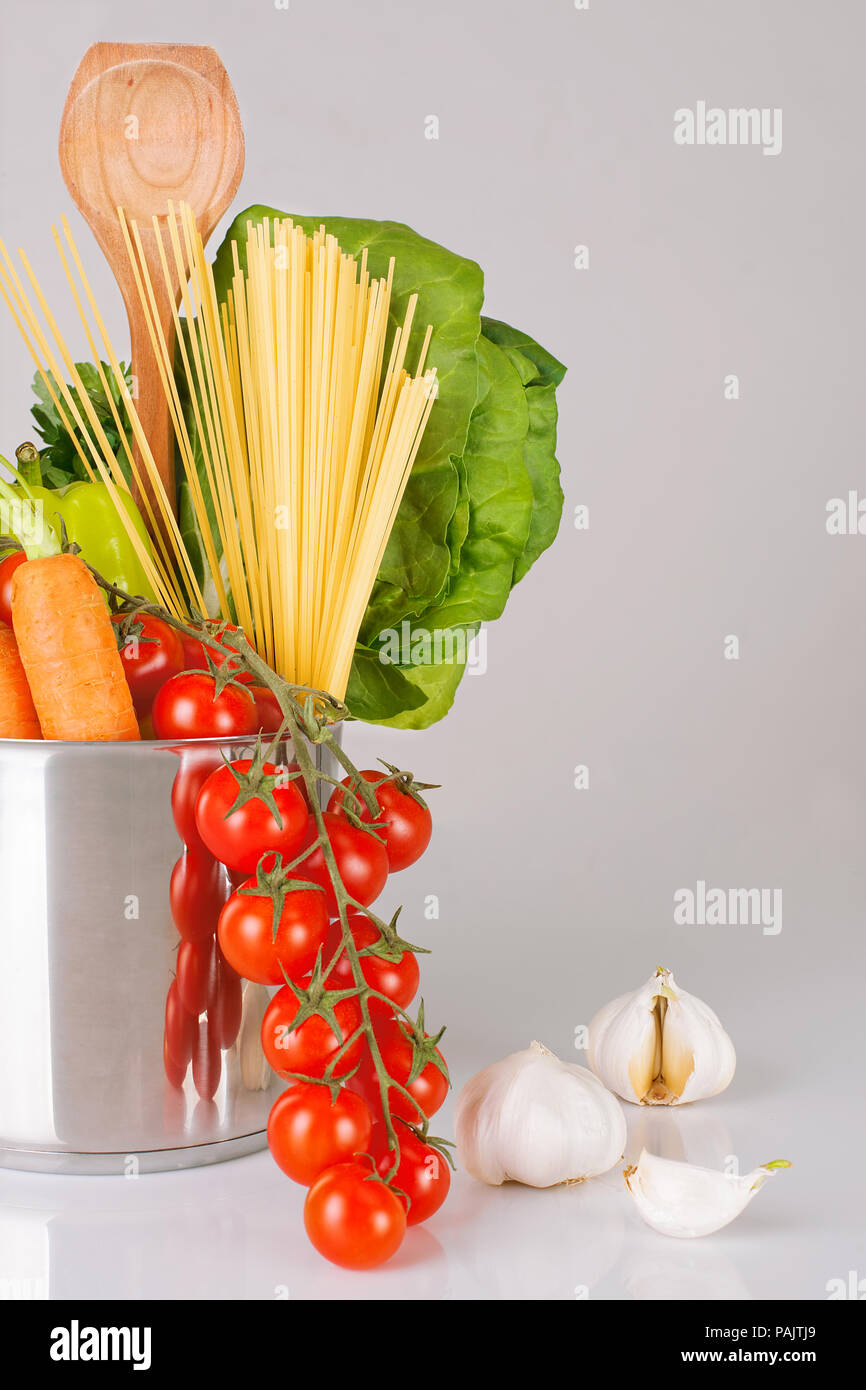 Varietà di verdure fresche, scoop e gli spaghetti al dente in una pentola di metallo su uno sfondo grigio, verticale, backround grigio Foto Stock
