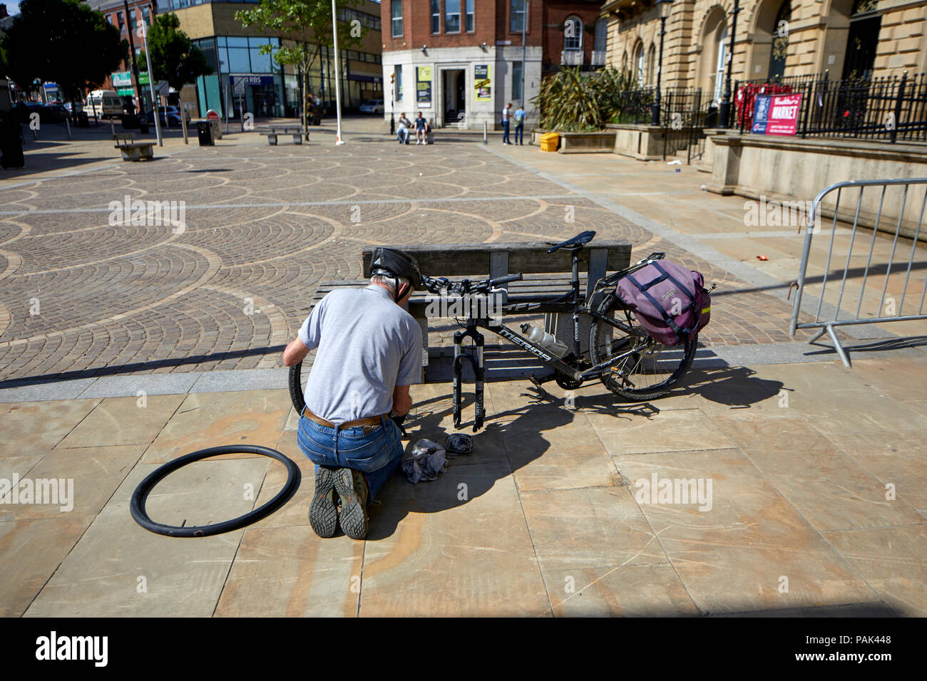 Blackbun Town Center in Lancashire, Inghilterra, il Municipio ciclista il fissaggio di un pneumatico forato sulla sua moto Foto Stock