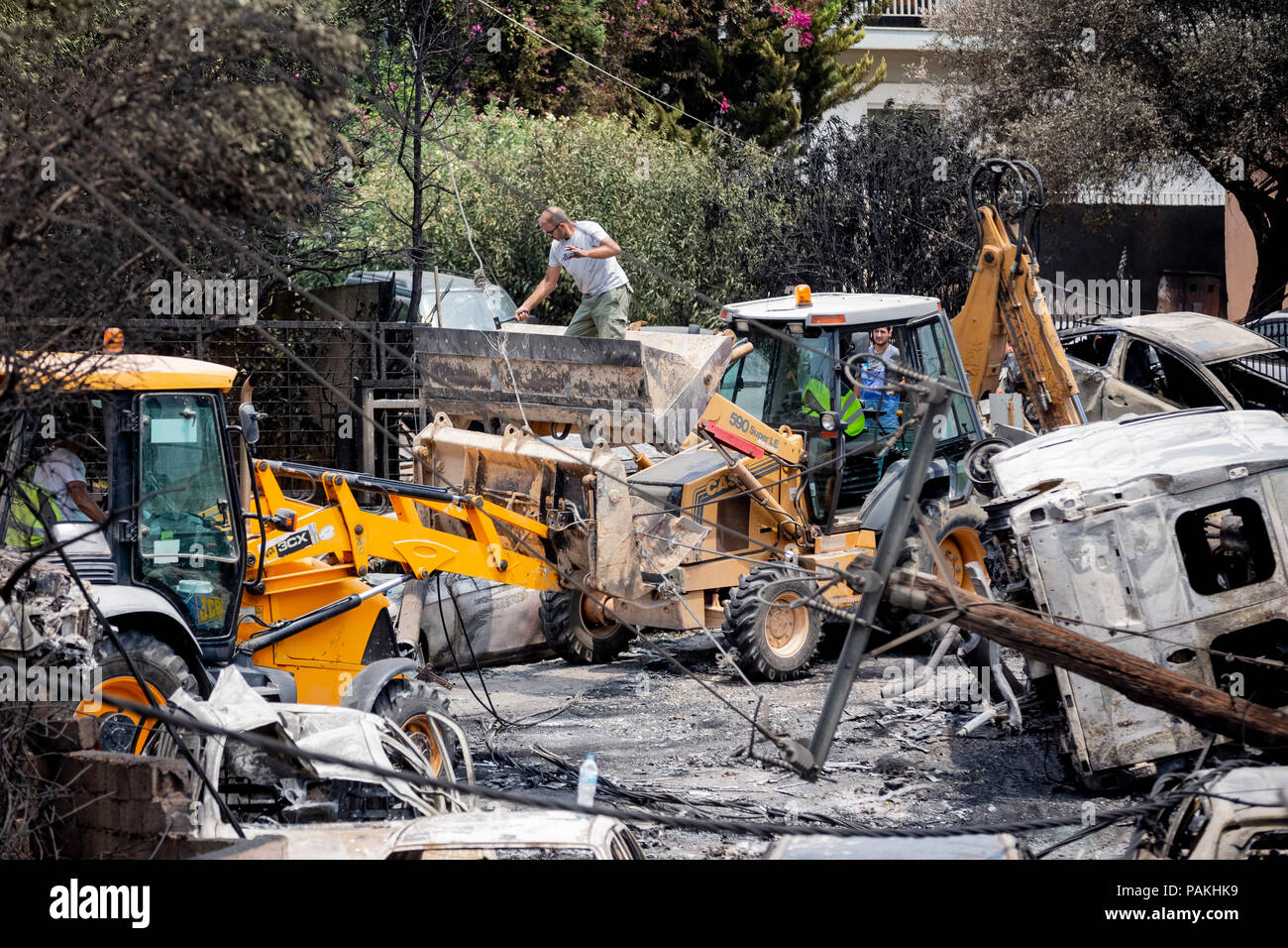 Mati, Grecia. Il 24 luglio, 2018. Un uomo in un escavatore pala taglia la linea di alimentazione di un montante di caduti per cancellare la strada dopo un incendio infuriò lì la notte scorsa. In base a nuove informazioni, il fuori-di-controllo degli incendi nei pressi di Atene ha ucciso diverse persone il 24 luglio 2018. Credito: Christoph Soeder/dpa/Alamy Live News Foto Stock