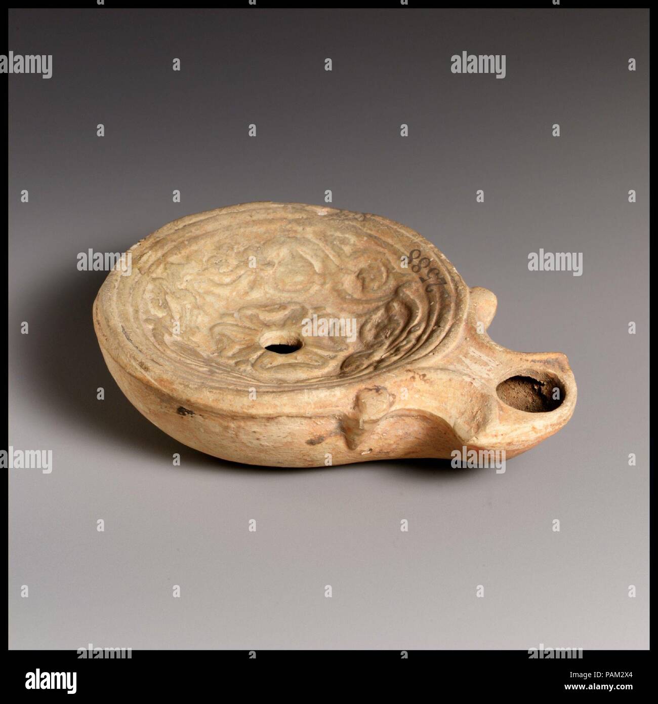 Olio di terracotta con lampada. Cultura: Romano. Dimensioni: complessivo: 1 1/8 x 3 7/8 in. (2,9 x 9,8 cm). Data: 1° secolo a.c.-1st secolo D.C.. Loeschcke tipo 1A. Stampo-fatta. Discus: una rosetta centrale con quattro grandi petali, circondato da un fregio di viticci con boccioli e fiori; un unico foro di riempimento al centro, con una fascia di linee e di scanalature in corrispondenza del bordo. Volute fiancheggianti ugello angolare, con un grande foro di stoppino. Base rialzata anello, con una ristretta cerchia sollevata all'interno e di un piano di base. Intatto. Museo: Metropolitan Museum of Art di New York, Stati Uniti d'America. Foto Stock