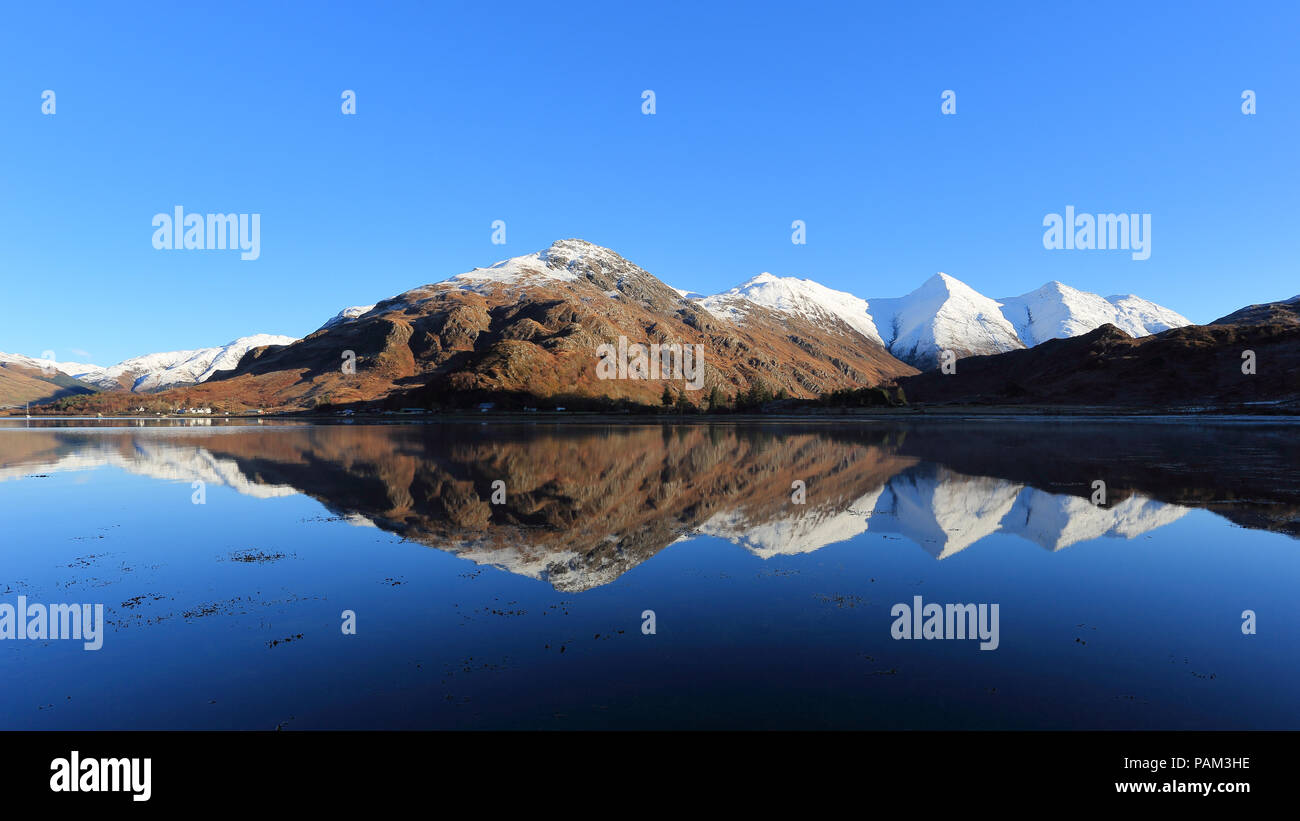 Spruzzata di neve montagne, le cinque sorelle di Kintail, riflettendo in Loch Duich Foto Stock