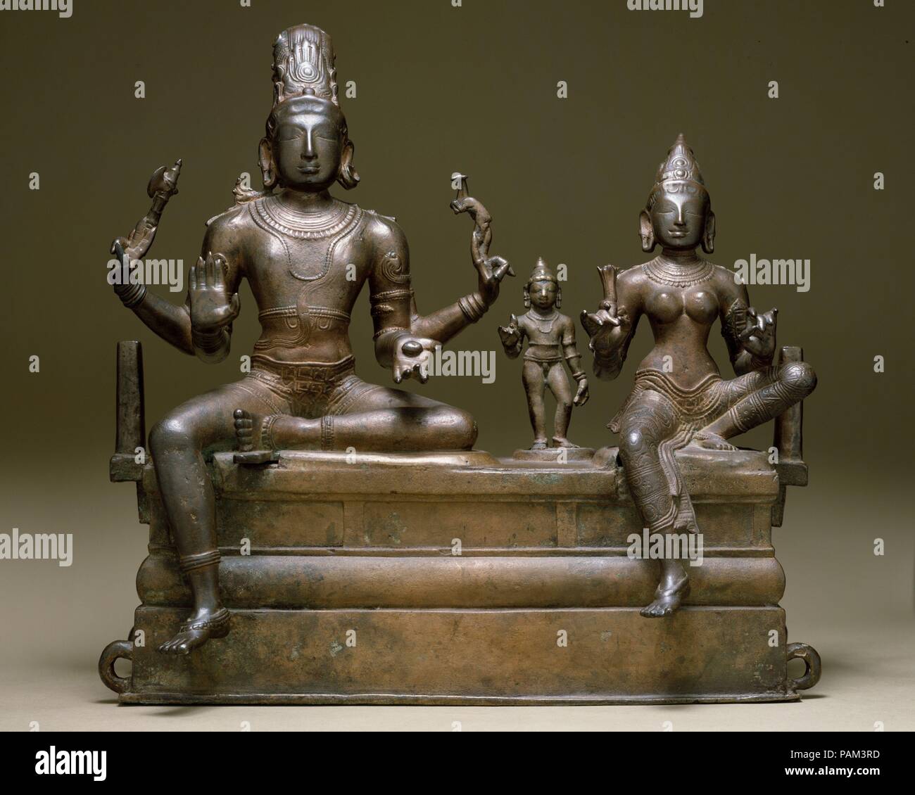 Shiva, Uma e il loro figlio Skanda (Somaskandamurti). Cultura: India (Tamil Nadu). Dimensioni: H. 29 7/8 in. (53 cm); W. 21 7/8 in. (55,6 cm); D. 10 1/4 in. (26,2 cm). Data: inizio del XI secolo. Somaskandamurti è uno dei più popolari di immagini religiose in India del Sud. I quattro armati di Shiva detiene una battaglia-ax e un cervo nella sua mano superiore e un cedro in suo inferiore sinistra. Il suo destro inferiore viene sollevata in abhayamudra (il gesto che risponde paura). La sua consorte, Parvati, fermagli un giglio di acqua nella sua mano destra. Tra di essi si erge Skanda, il loro figlio bambino, bejeweled e con una Lotus nel suo diritto Foto Stock