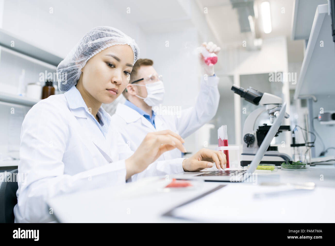 Ritratto di due moderni scienziati che studiano materie durante il lavoro di ricerca in laboratorio di analisi mediche, concentrarsi sul giovane donna asiatica nella parte anteriore Foto Stock