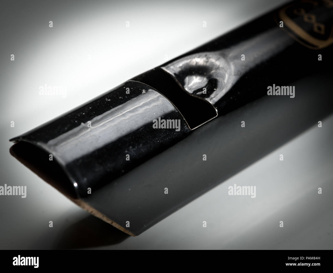 Dettagli di un nero tin whistle giacente su un bianco superficie riflettente Foto Stock