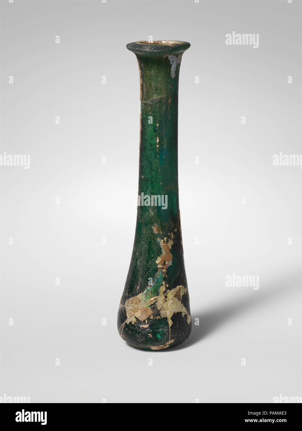 Il vetro della bottiglia di profumo. Cultura: Romano. Dimensioni: complessivo: 5 3/8 x 1 7/16 x 1 1/16 in. (13,7 x 3,7 x 2,7 cm). Data: 1a-2a secolo D.C.. Traslucido blu profondo verde. Cerchione piegato fuori, oltre e con superficie superiore schiacciato piatto; leggermente la svasatura di imbocco; tall collo cilindrico, con lati concavi, si espande verso il basso per entrare a far parte in maniera impercettibilmente corpo conico; fondo irregolare, con jagged pontil cicatrice. Completa ma rotti e riparati intorno al collo superiore ed inferiore del corpo; pinprick e bolle di forma allungata e striature di soffiaggio; profonda pitting, opacizzazione, e patch di brillanti iridescenza di esterno, suolo encru Foto Stock