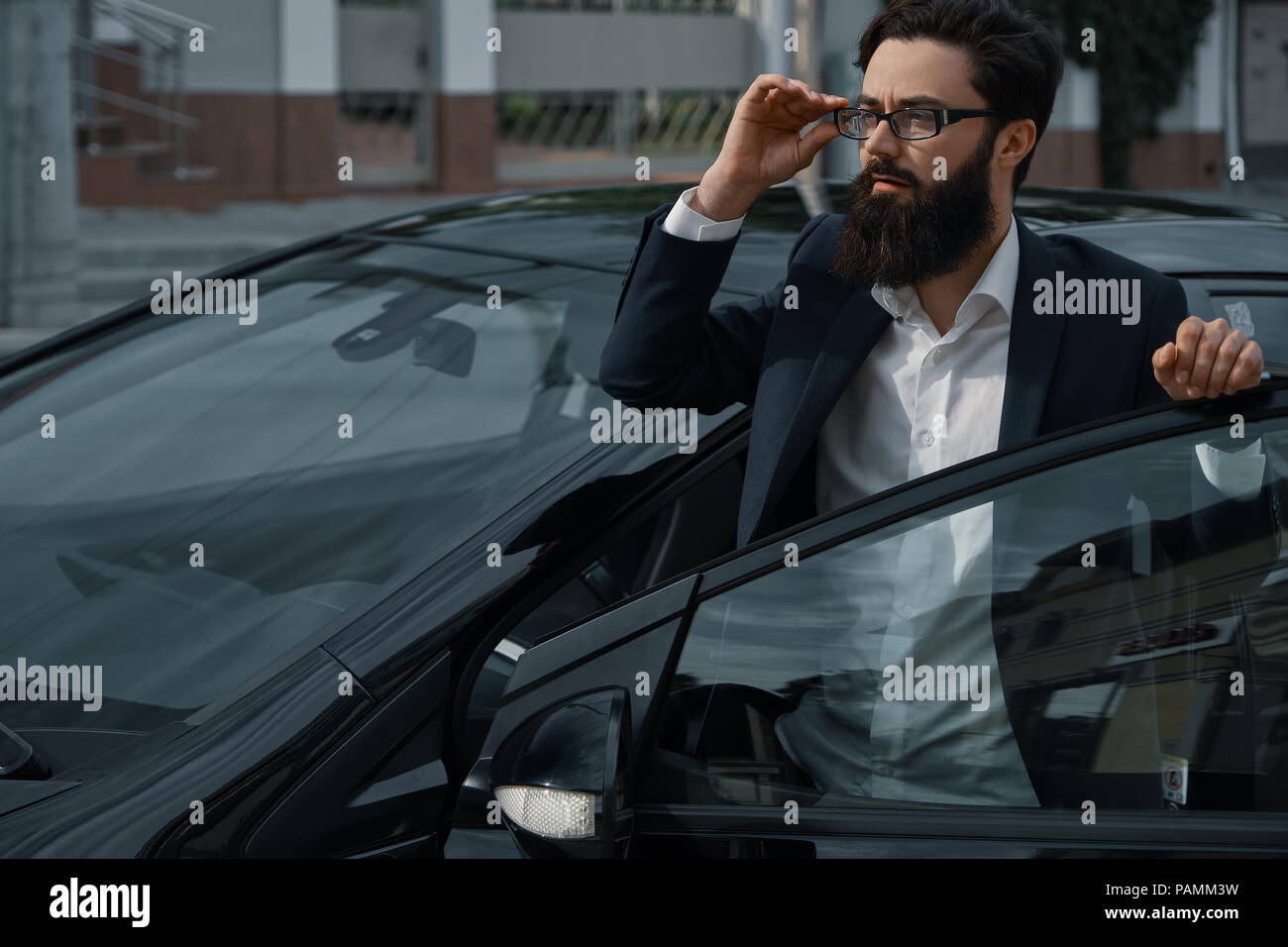 Fiducioso uomo in abbigliamento formale tenendo la mano aperta sulla porta auto wat Foto Stock