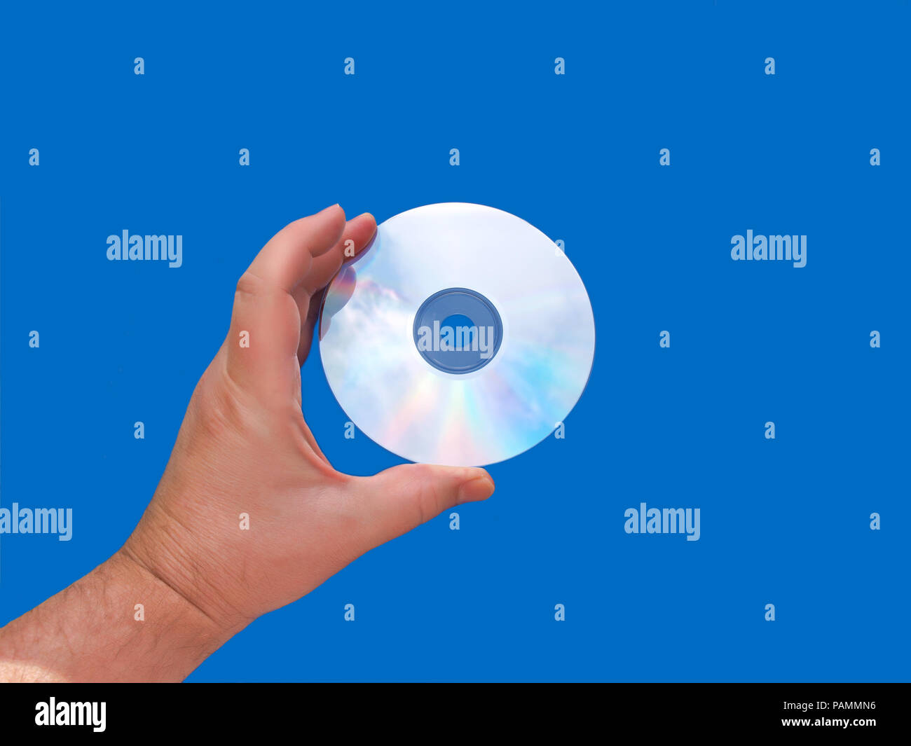 Una mano che tiene un sole illuminava i supporti CD o DVD che riflette il cielo contro uno sfondo blu Foto Stock
