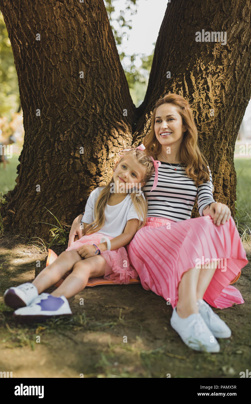 Donna sorridente indossare gonna rosa seduta vicino a sua figlia Foto Stock