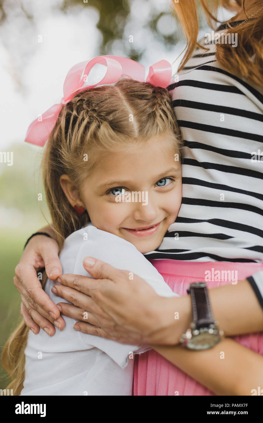 Bionda madre indossa striped shirt abbracciando la sua ragazza carina Foto Stock