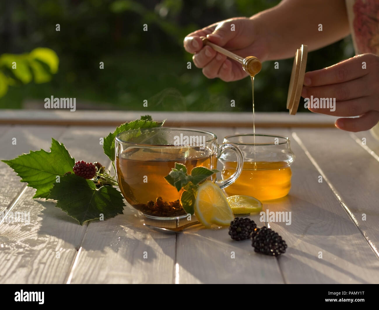 Concetto di colazione sana. Vita lenta. Tè con limone, frutti di bosco e miele in vaso. La donna sta raccogliendo il miele Foto Stock