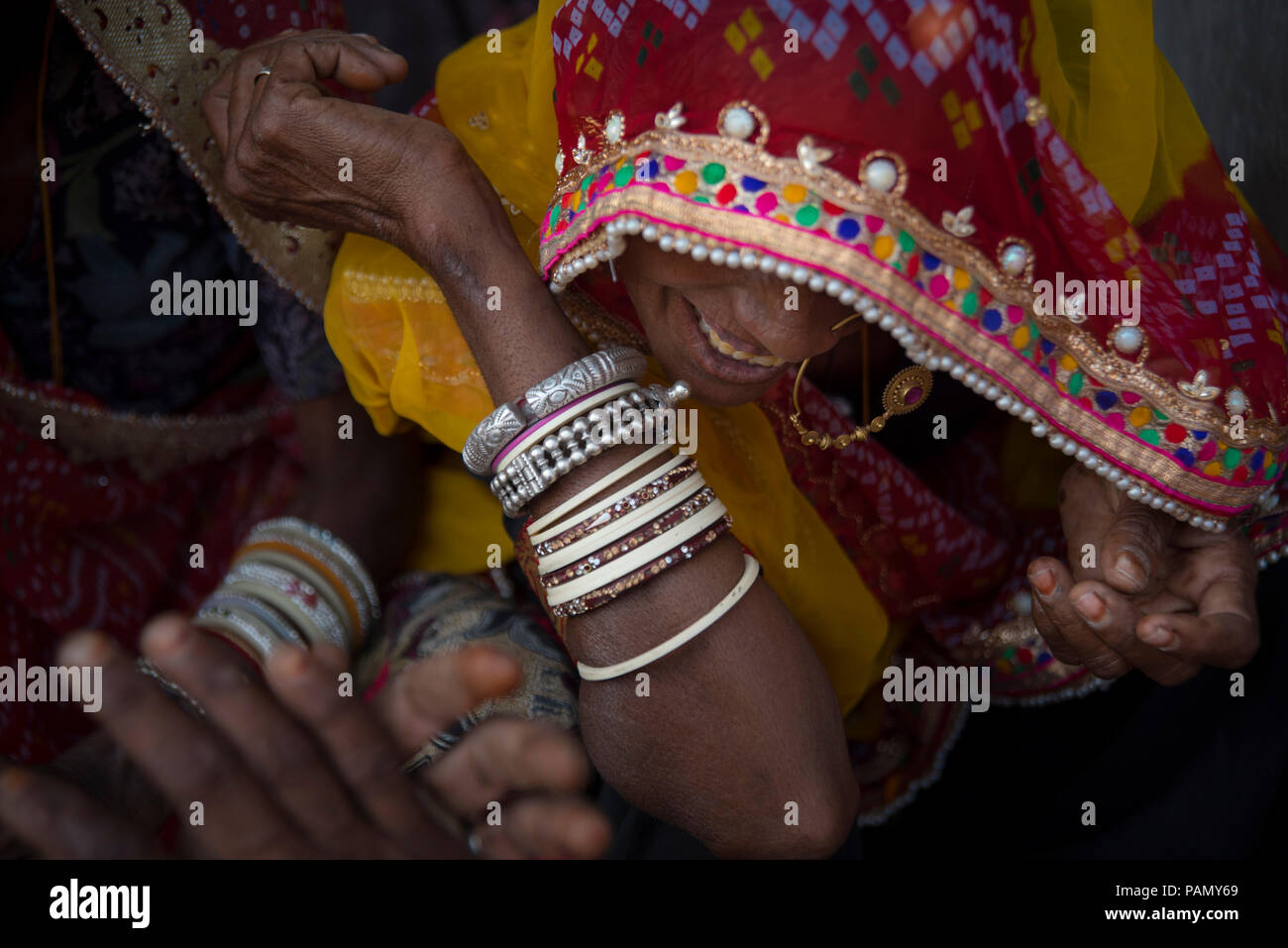 Donna indiana sorridente, indossando un dorato anello di naso, un rosso e senape foulard ricamati e molti braccialetti. 4 mani nel telaio. Foto Stock