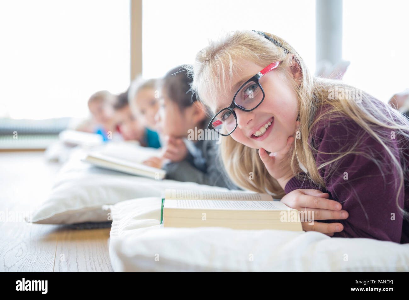 Ritratto di sorridere schoolgirl sdraiato sul pavimento con i compagni di classe la lettura di libri di scuola in sala pausa Foto Stock
