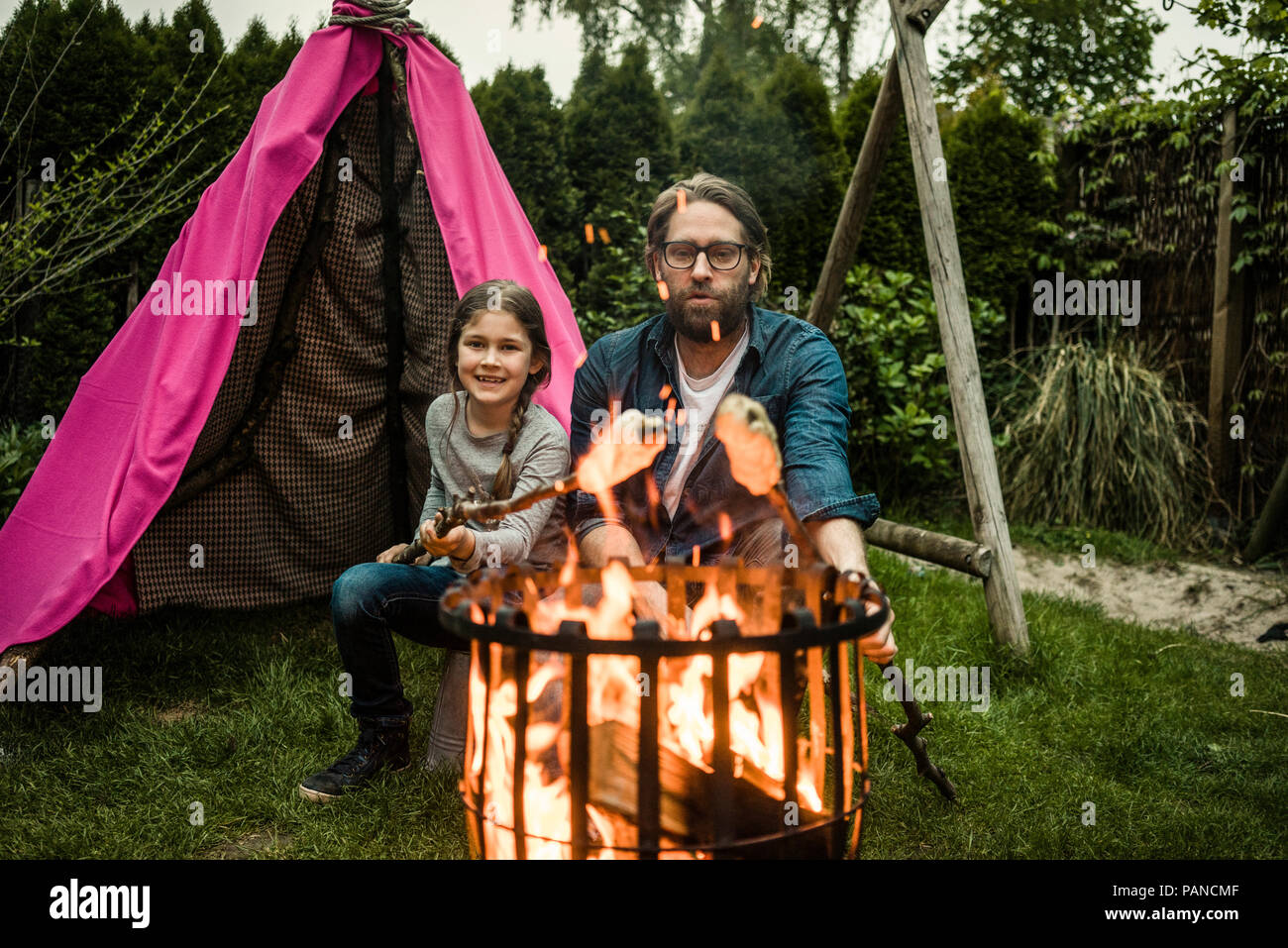 Padre e figlia di grigliatura pane di torsione su fuoco di campo Foto Stock