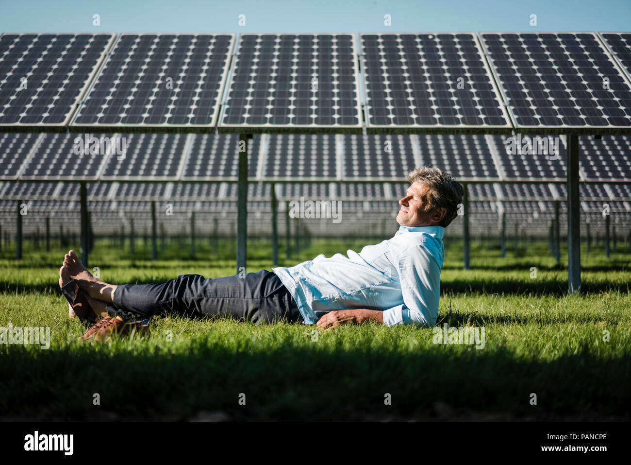 Uomo maturo giacente a piedi nudi sul prato, impianto solare Foto Stock