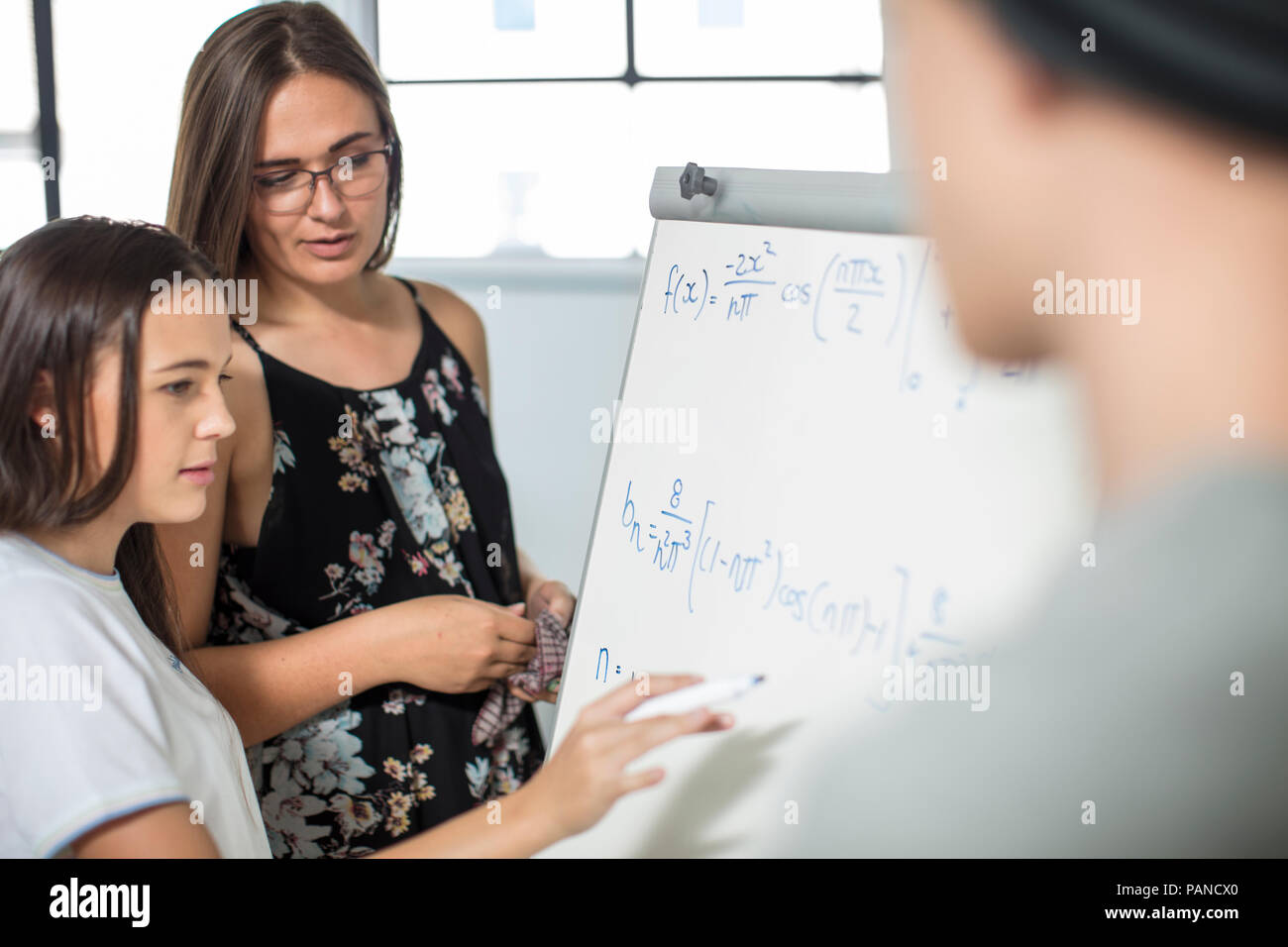 Docente aiutare ragazza adolescente formula di scrittura su whiteboard Foto Stock