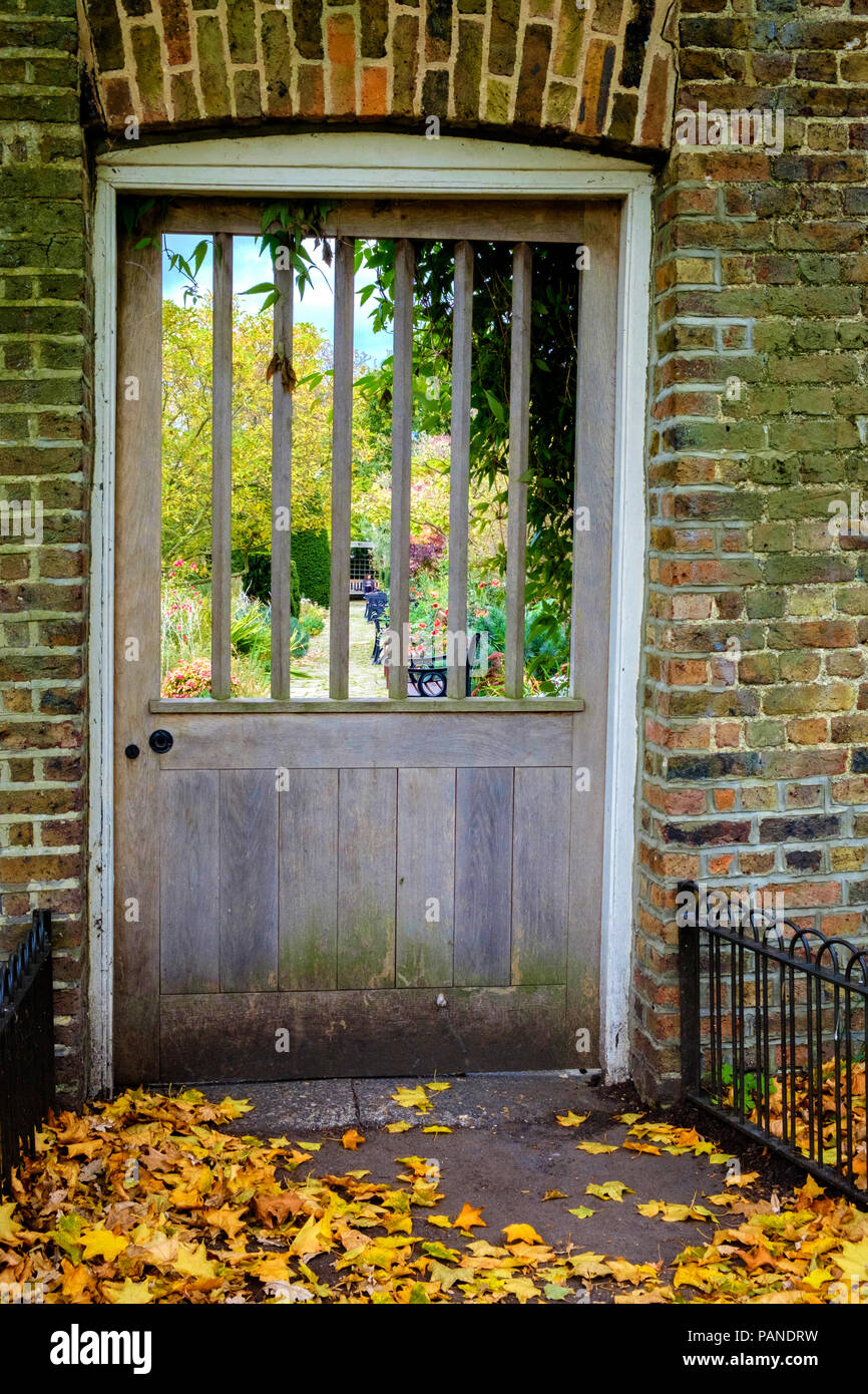 Porta in legno con asole cercando in giardino murato nel Brockwell Park, Herne Hill Londra Sud, Regno Unito. Giallo caduto foglie di autunno sul terreno. Ritratto. Foto Stock