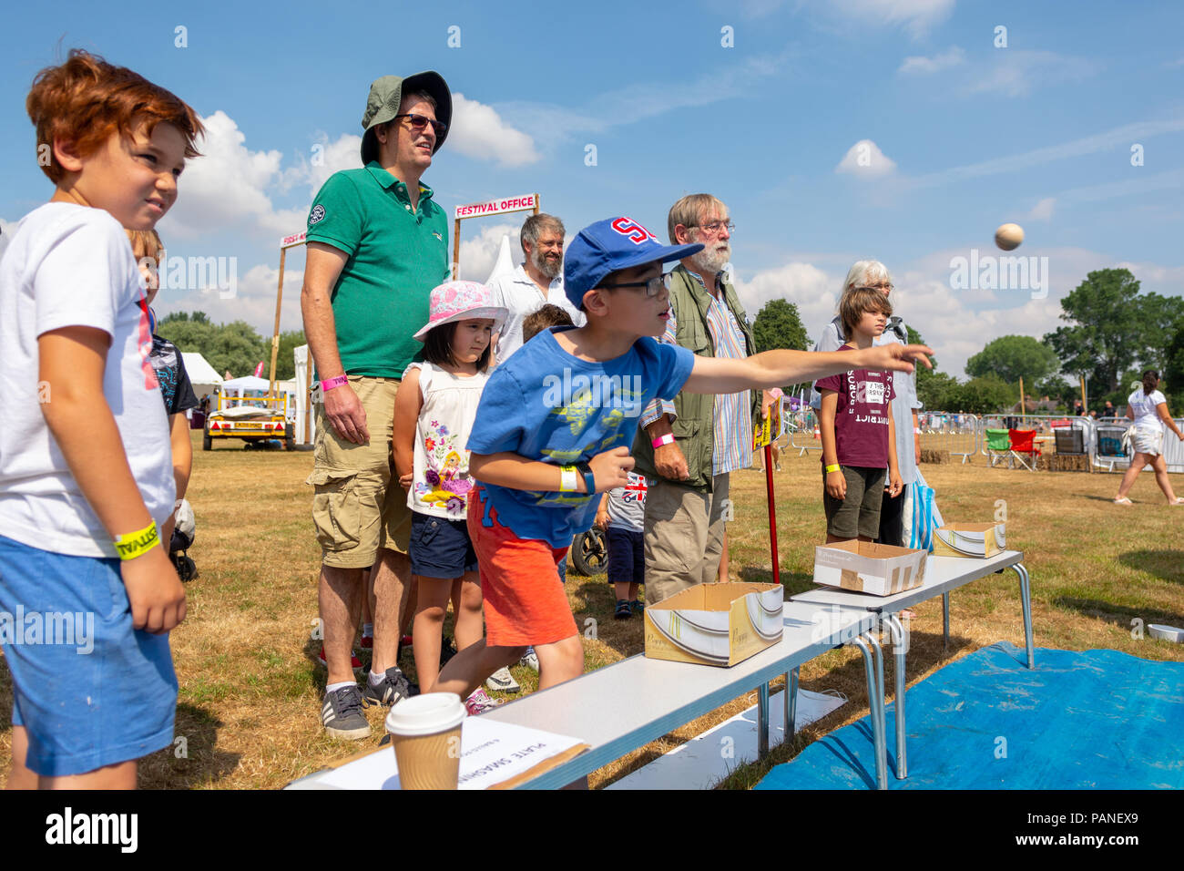 Ragazzo in una capsula di chiusura di colore blu e t-shirt di gettare una palla di legno in corrispondenza di una piastra smashing stallo a una fiera di paese in Hampshire Foto Stock