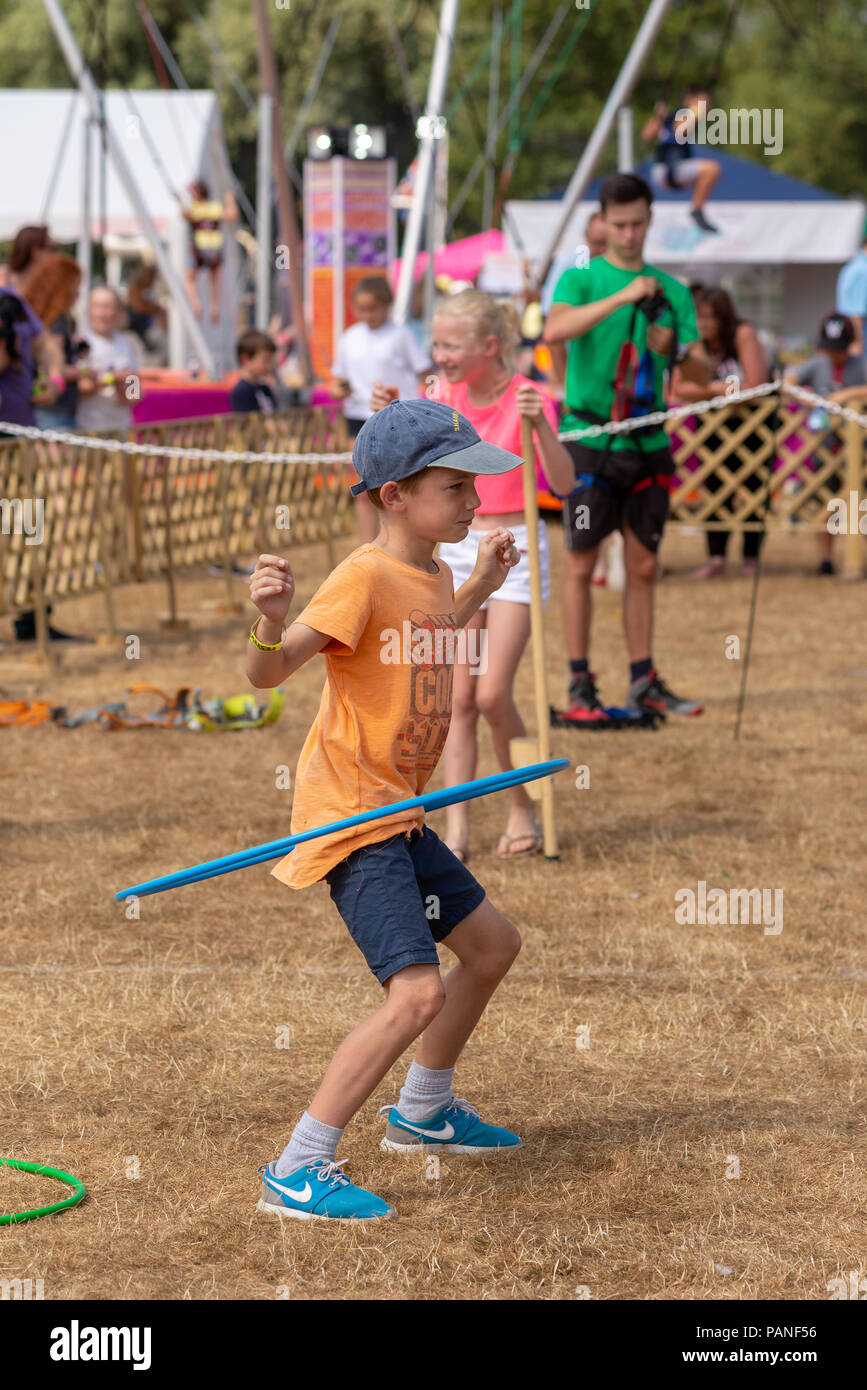 Ragazzo in una t-shirt, un tappo blu e blu dei formatori utilizzando un-hula hoop a una fiera di paese in Hampshire Foto Stock