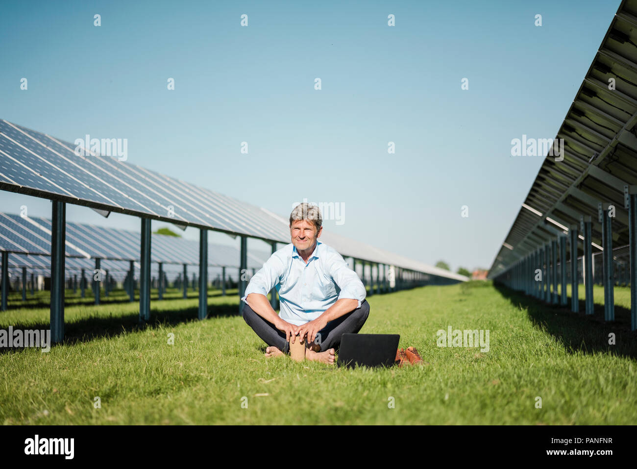 Coppia uomo seduto a piedi nudi sul prato, laptop e caffè di andare cup, impianto solare Foto Stock