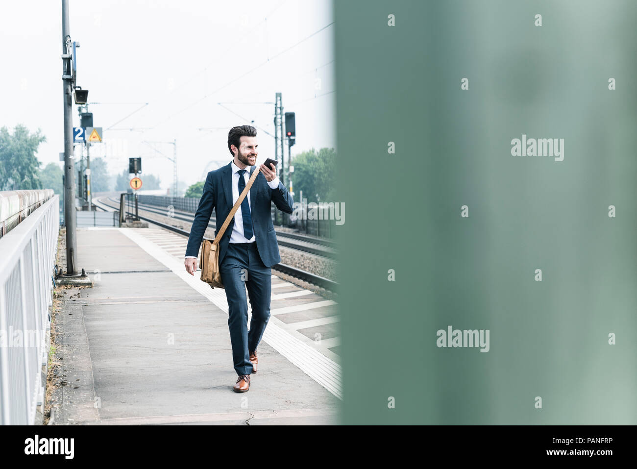Imprenditore sorridente con un telefono cellulare a piedi a piattaforma Foto Stock