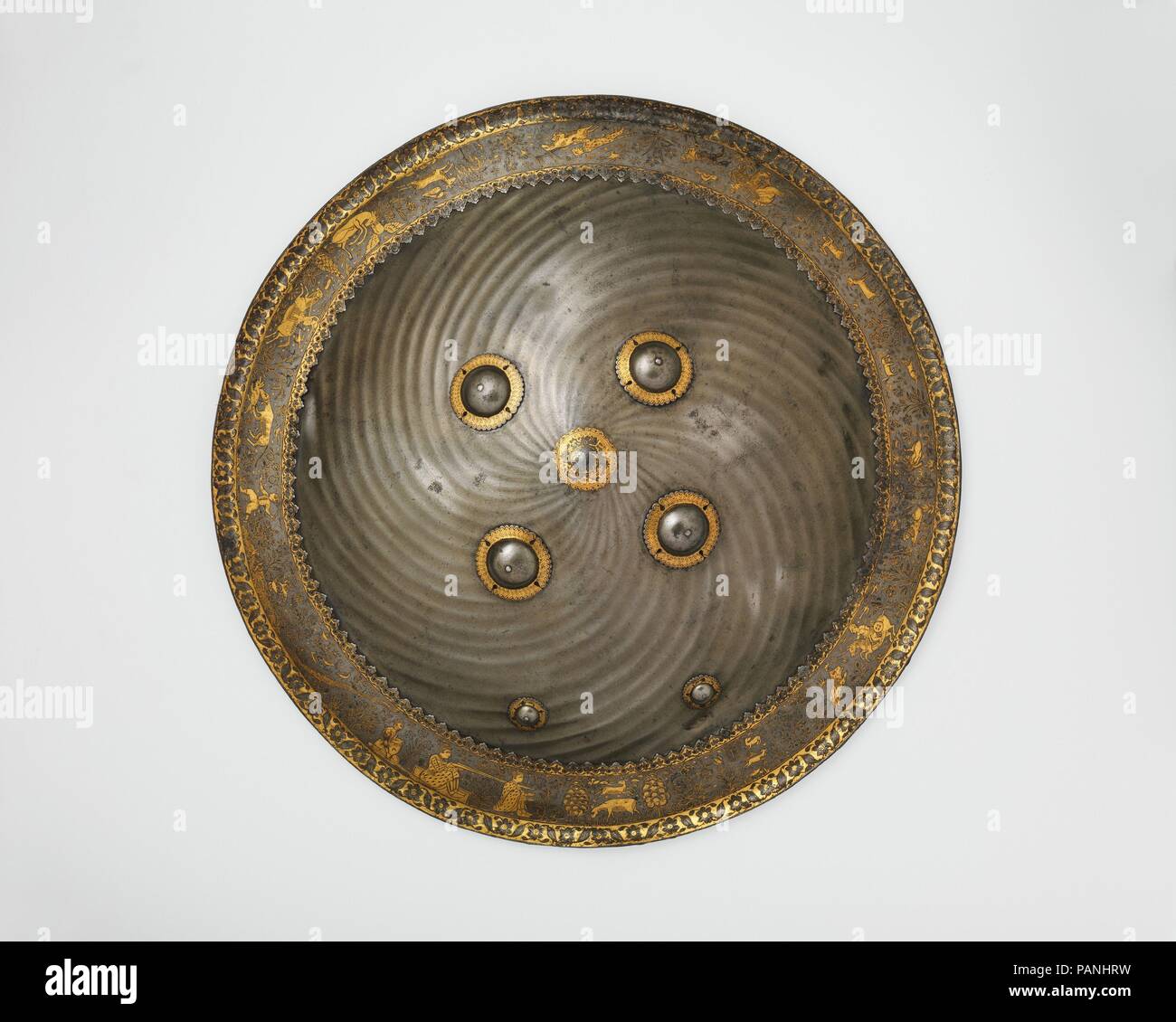 Protezione con la caccia e il paesaggio vignette. Dimensioni: diam. 21 11/16 in. (57,7 cm). Data: seconda metà del XVII secolo. L Mughal estetica sono riflesse nel suo armamento. Questa protezione, che appartiene al primo quarto del XVIII secolo, è riccamente decorato con intarsi decorazioni in oro sul suo bordo e la manopola. Il soggetto raffigurato sul bordo del cerchio mostra il righello che è accompagnato dai suoi servi' mira con il suo fucile, galoppa su un cavallo con una lancia in mano o attacchi di una furiosa lion. La caccia scena raffigura il movimento dinamico con cani e tiger salto sulla loro preda e un Foto Stock