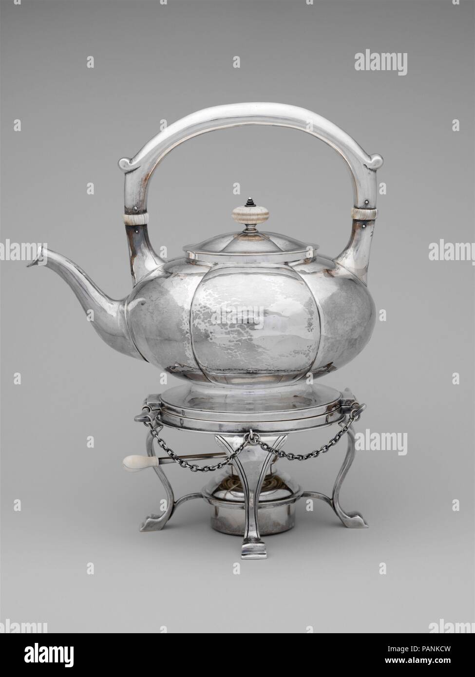 Teakettle sul supporto. Cultura: American. Dimensioni: 11 x 9 in. (27,9 x 22,9 cm). Autore: James T. Woolley (1864-dopo il 1927). Data: ca. 1910. Avendo lavorato per molti anni per la Boston argentieri Goodnow e Jenks, Woolley ha stabilito la sua bottega nel 1908. Uno dei primi membri e premiata medaglia di Boston la Società delle Arti e mestieri, anche egli apparteneva alla società di Detroit di arti e mestieri ed espone a New York City. Molto del Woolley's lavoro riflette il Colonial Revival stile, come esemplificato in questo scanalate, teakettle sferica su supporto. Museo: Metropolitan Museum of Art di New Yor Foto Stock