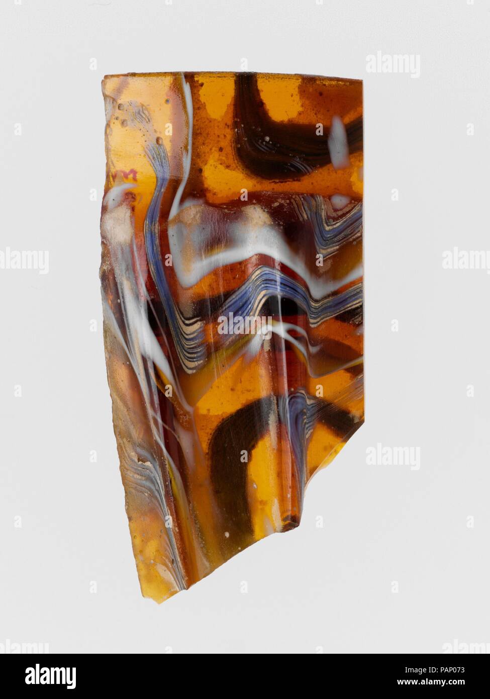 Mosaico di vetro scanalata frammento di ciotola. Cultura: Romano. Dimensioni: complessivo: 2 1/2 x 1 3/16 in. (6,4 x 3 cm). Data: fine del I secolo A.C. - inizio del I secolo d.c. Frammento di RIM. Miele traslucido marrone, blu cobalto, blu e bianco opaco. Leggermente rovesciata con bordo arrotondato il labbro interno; in alto, laterali rastremantesi procedendo verso il basso, quindi il rigonfiamento verso l'esterno con curvatura convessa profilo. Nastro mosaico formata da spezzoni di una o più canne in un marrone terra ondulata con bianco e blu thread in parallelo le linee; sulla parte esterna, due verticali sottili nervature, con sommità appiattita e spigoli esterni arrotondati, rastremata verso il basso. Poli Foto Stock