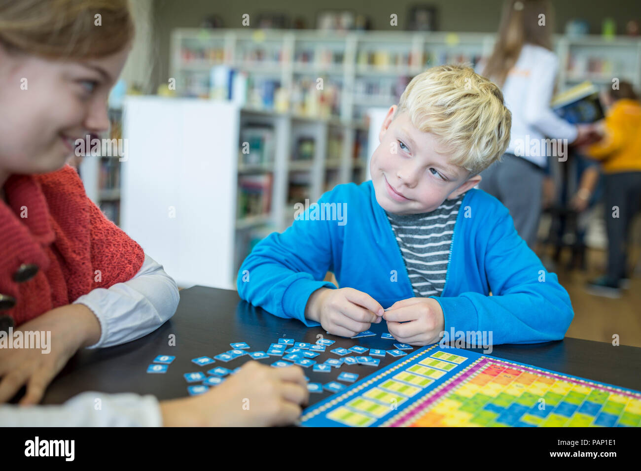 Gli alunni la riproduzione di un gioco di bordo in biblioteca scolastica sorridente ad ogni altro Foto Stock