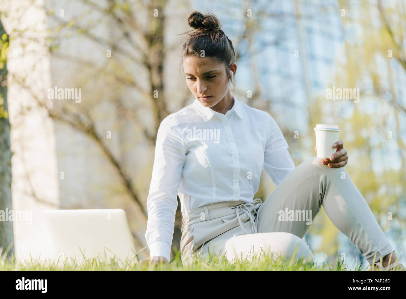 Giovane imprenditrice prendendo break, utilizzando laptop, seduta in erba e di bere il caffè Foto Stock