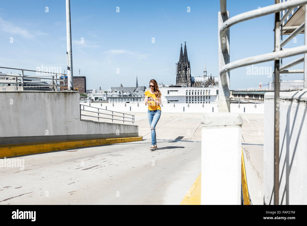 Germania, Colonia, Donna che cammina sulla rampa del packing livello tramite il telefono cellulare Foto Stock