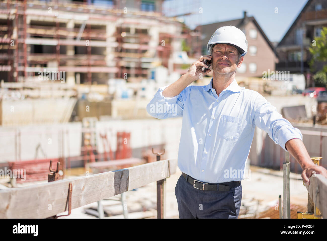 Uomo che indossa il casco sul cellulare sul sito in costruzione Foto Stock