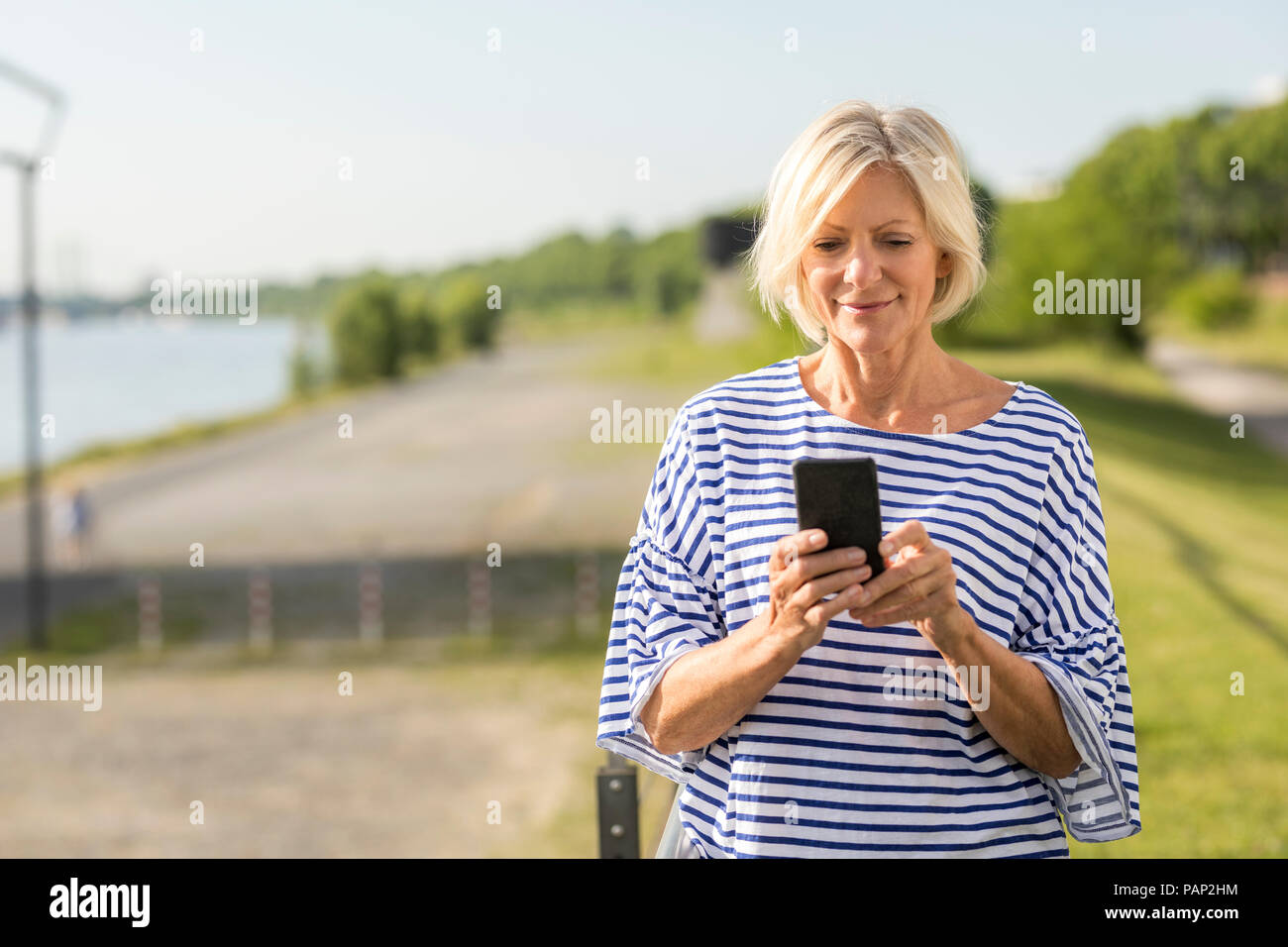 Sorridente donna senior tramite telefono cellulare a riverbank Foto Stock